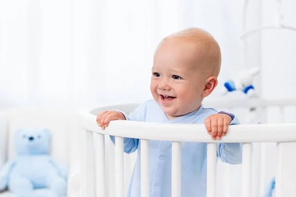 Baby boy standing in bed in white nursery — Stock Photo, Image