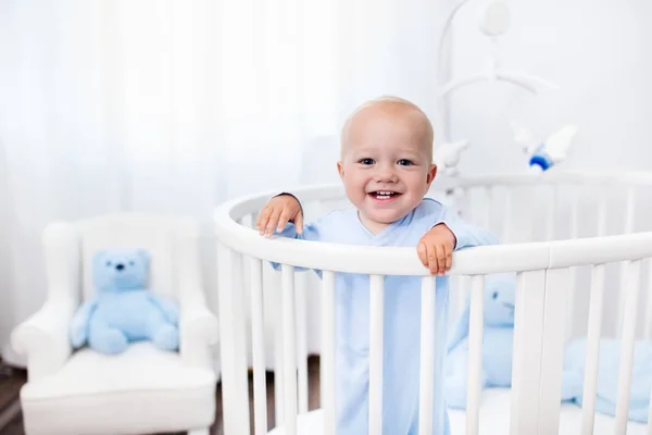 Baby boy standing in bed in white nursery — Stock Photo, Image