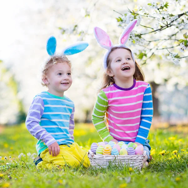 Caza de huevos de Pascua. Niños con orejas de conejo en jardín de primavera . — Foto de Stock