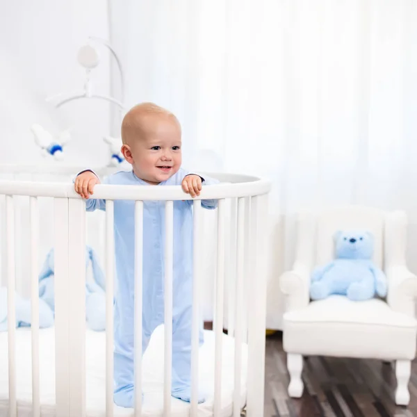 Baby boy standing in bed in white nursery — Stock Photo, Image