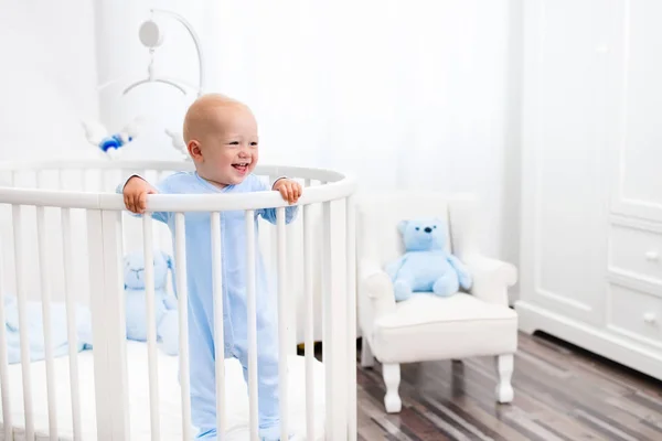 Baby boy standing in bed in white nursery — Stock Photo, Image