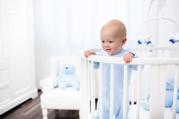 Baby boy standing in bed in white nursery — Stock Photo, Image