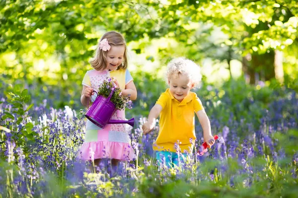 Děti hrají v kvetoucí zahradě květinami bluebell — Stock fotografie