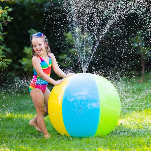 Vicces nevető kis lány játszik a játék labda kerti megszórjuk színes swimming-suit — Stock Fotó
