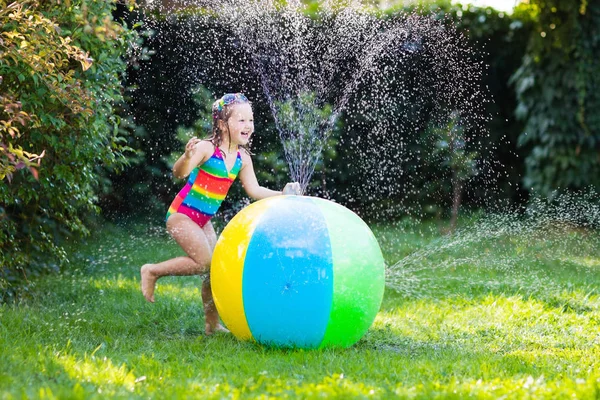 Little girl in a colorful swimming suit playing with toy ball garden sprinkler