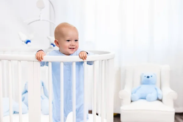 Baby boy standing in bed in white nursery — Stock Photo, Image