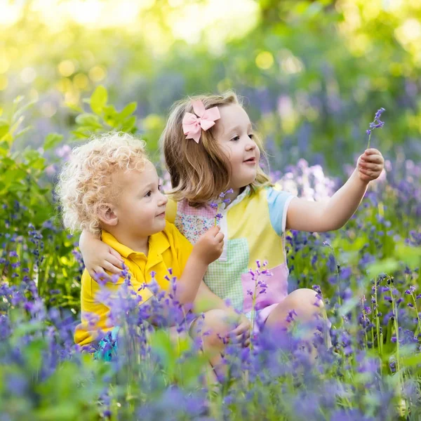 Děti hrají v kvetoucí zahradě květinami bluebell — Stock fotografie