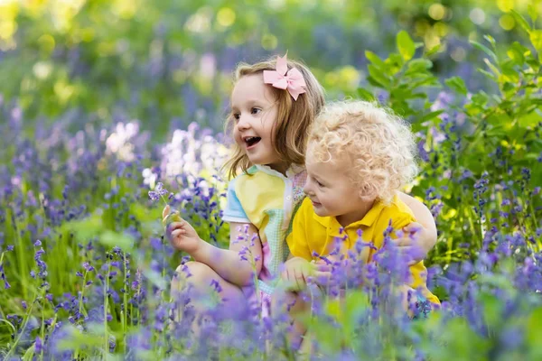 Děti hrají v kvetoucí zahradě květinami bluebell — Stock fotografie