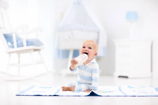 Baby boy drinking milk in sunny nursery — Stock Photo, Image
