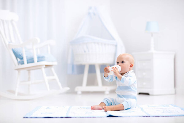 Малыш пьет молоко в солнечной детской.
