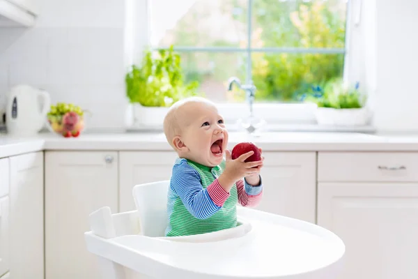 Baby pojke äta äpple i vitt kök hemma — Stockfoto