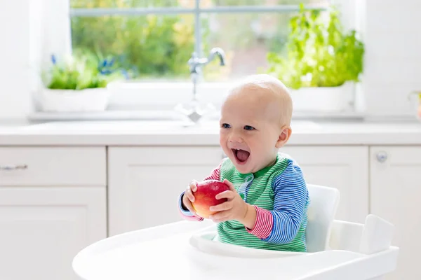 Menino comendo maçã na cozinha branca em casa — Fotografia de Stock