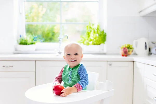 Menino comendo maçã na cozinha branca em casa — Fotografia de Stock