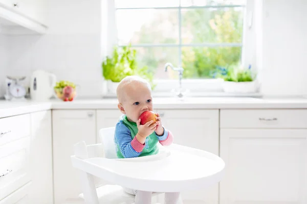 Menino comendo maçã na cozinha branca em casa — Fotografia de Stock