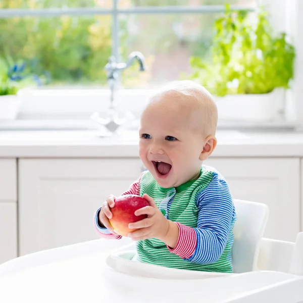 Baby boy eating apple in white kitchen at home — Stock Photo, Image