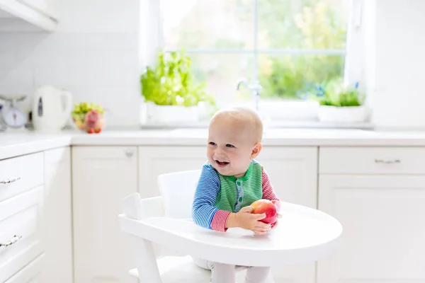 Baby boy jedzenia apple w biały kuchnia w domu — Zdjęcie stockowe