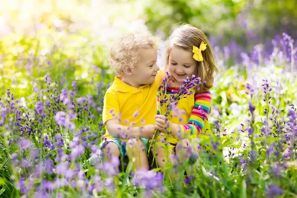 Děti hrají v kvetoucí zahradě květinami bluebell — Stock fotografie