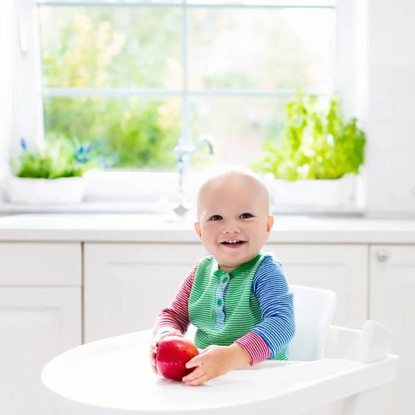 Menino comendo maçã na cozinha branca em casa — Fotografia de Stock