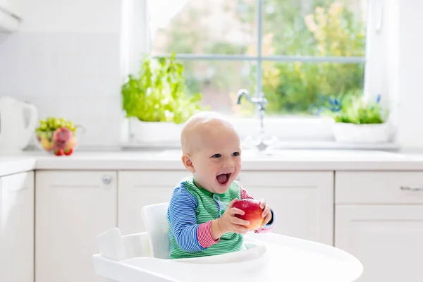 Menino comendo maçã na cozinha branca em casa — Fotografia de Stock