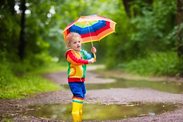 Niño jugando bajo la lluvia bajo paraguas — Foto de Stock