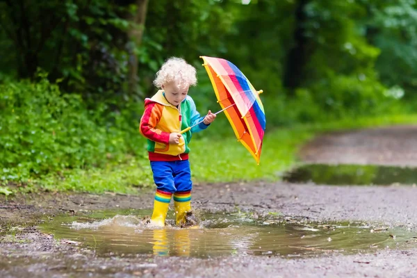 Niño jugando bajo la lluvia bajo paraguas — Foto de Stock