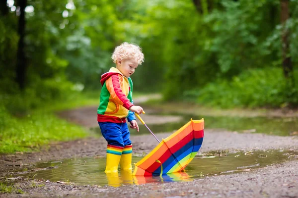 Niño jugando bajo la lluvia bajo paraguas — Foto de Stock