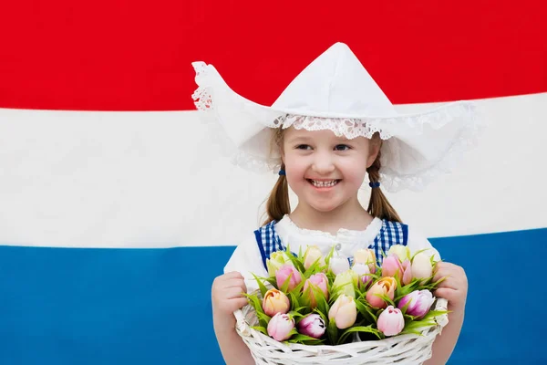 Holandská dítě s tulipánu květin a Nizozemsko vlajka — Stock fotografie