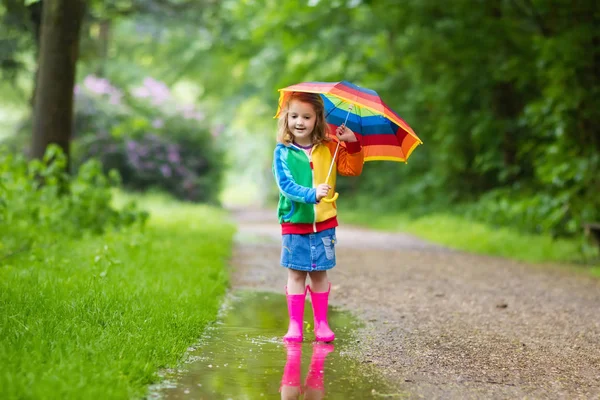Ребенок играет под дождем с зонтиком — стоковое фото