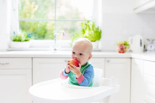 Дитячий хлопчик їсть яблуко на білій кухні вдома — стокове фото
