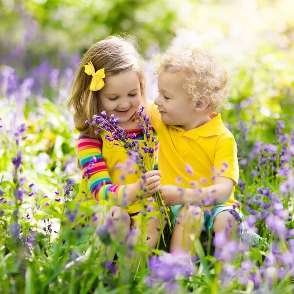 Děti hrají v kvetoucí zahradě květinami bluebell — Stock fotografie