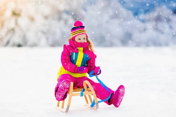 Child playing in snow on sleigh in winter park — Stock Photo, Image