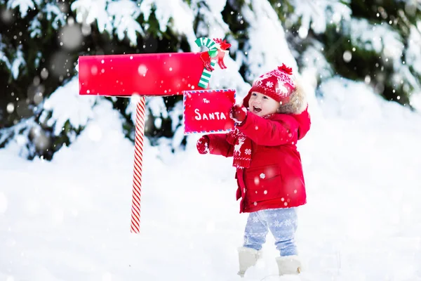 Dítě s dopis do Santa na Vánoce mail box ve sněhu — Stock fotografie