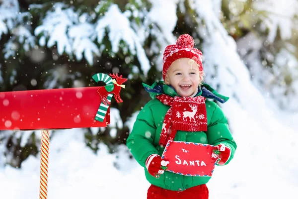 Criança com carta ao Papai Noel na caixa de correio de Natal na neve — Fotografia de Stock