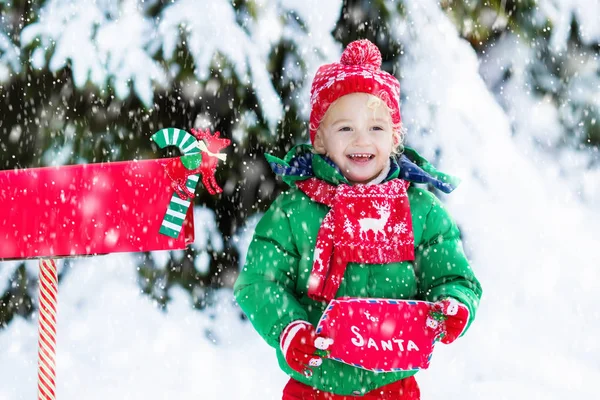 Criança com carta ao Papai Noel na caixa de correio de Natal na neve — Fotografia de Stock