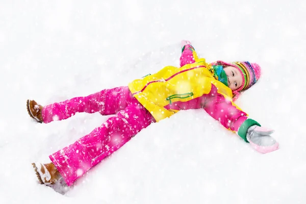 Child making snow angel. Kids play in winter park.