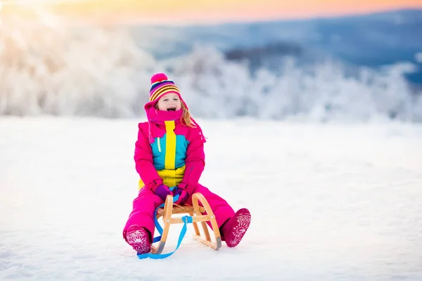 Bambino che gioca sulla neve sulla slitta nel parco invernale — Foto Stock
