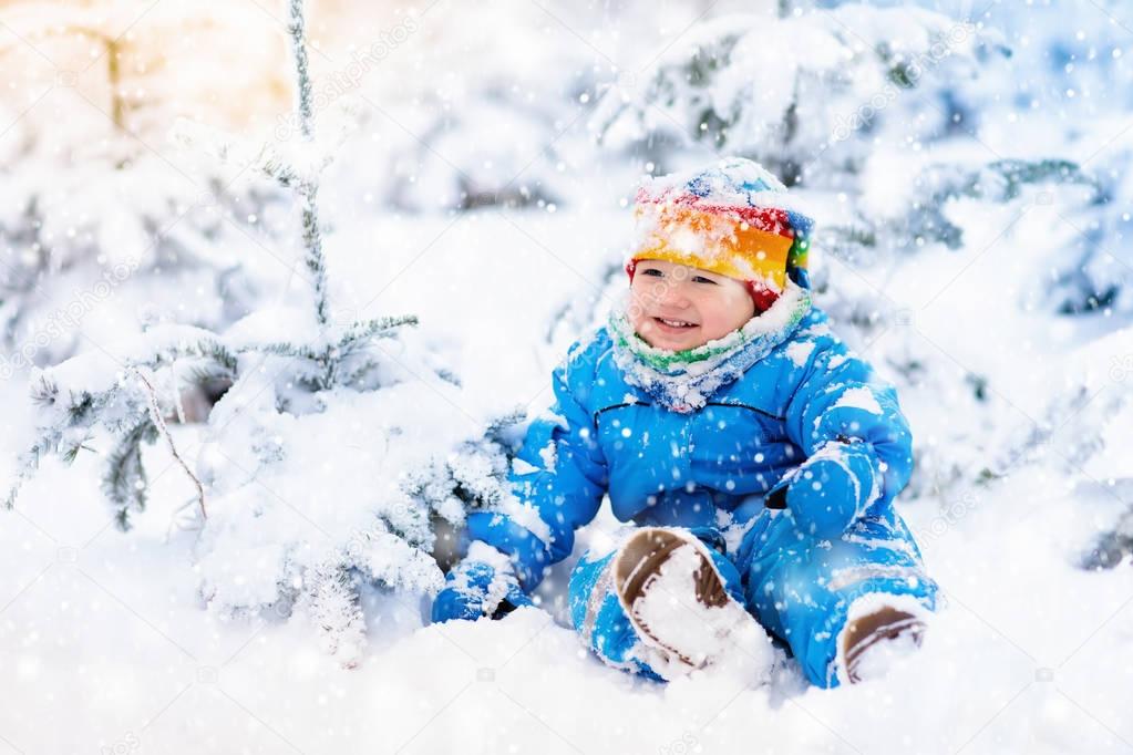 Baby playing with snow in winter. Child in snowy park.