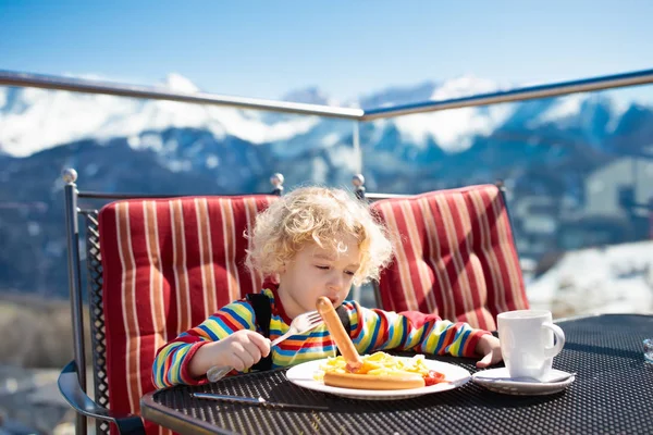 Criança comendo apres almoço de esqui. Inverno neve diversão para crianças . — Fotografia de Stock