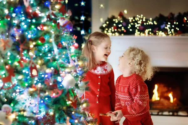 Τα παιδιά στο χριστουγεννιάτικο δέντρο. Τα παιδιά στο τζάκι την παραμονή των Χριστουγέννων — Φωτογραφία Αρχείου