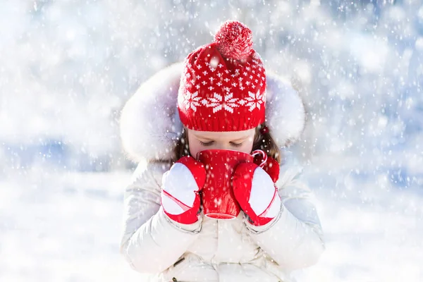 Child drinking hot chocolate in winter park. Kids in snow on Chr