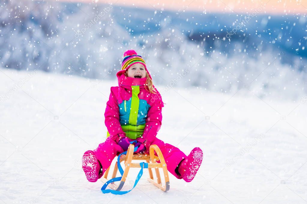 Child playing in snow on sleigh in winter park