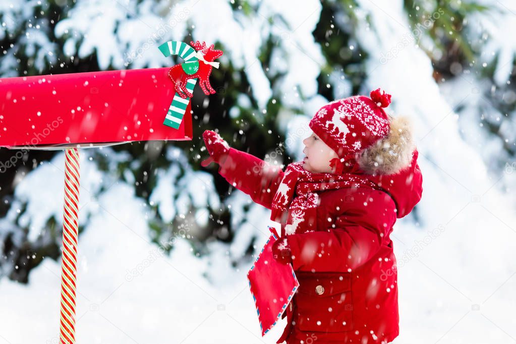 Child with letter to Santa at Christmas mail box in snow