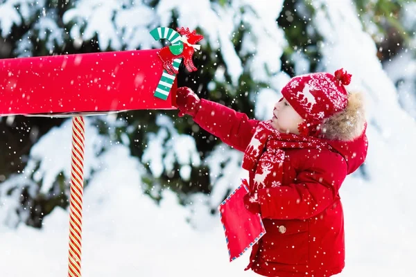 Criança com carta ao Papai Noel na caixa de correio de Natal na neve — Fotografia de Stock
