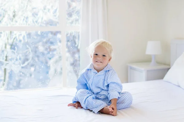 Niño en la cama. Ventana de invierno. Niño en casa por la nieve . —  Fotos de Stock