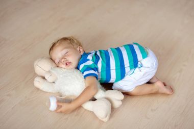Oyuncak ve süt şişesiyle katta uyuyan bebek.