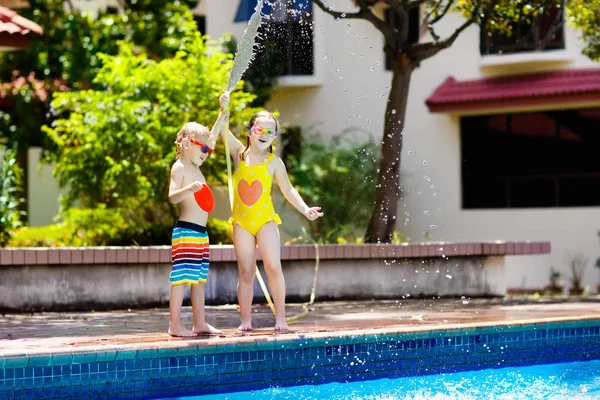 Kids play with water hose at swimming pool.