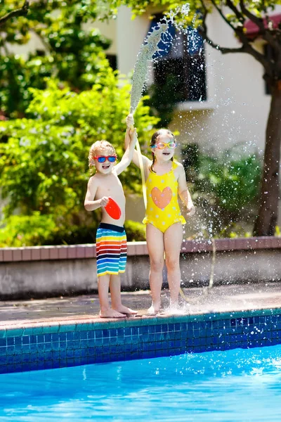 Unger leker med vannslange i svømmebassenget. . – stockfoto