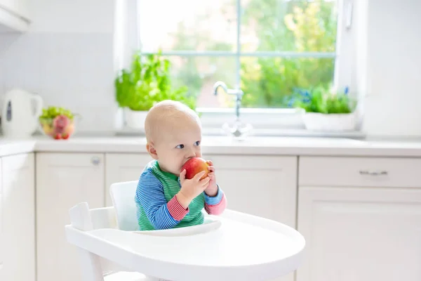 Малыш ест яблоко на белой кухне дома — стоковое фото