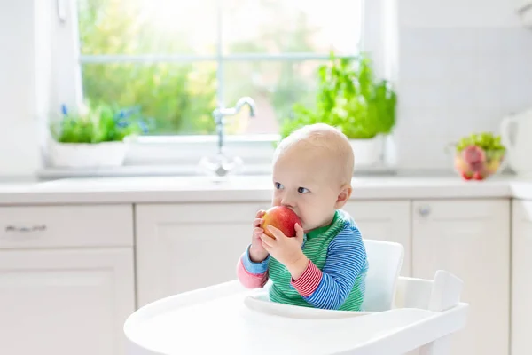 Baby pojke äta äpple i vitt kök hemma — Stockfoto