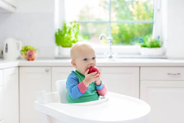 Малыш ест яблоко на белой кухне дома — стоковое фото